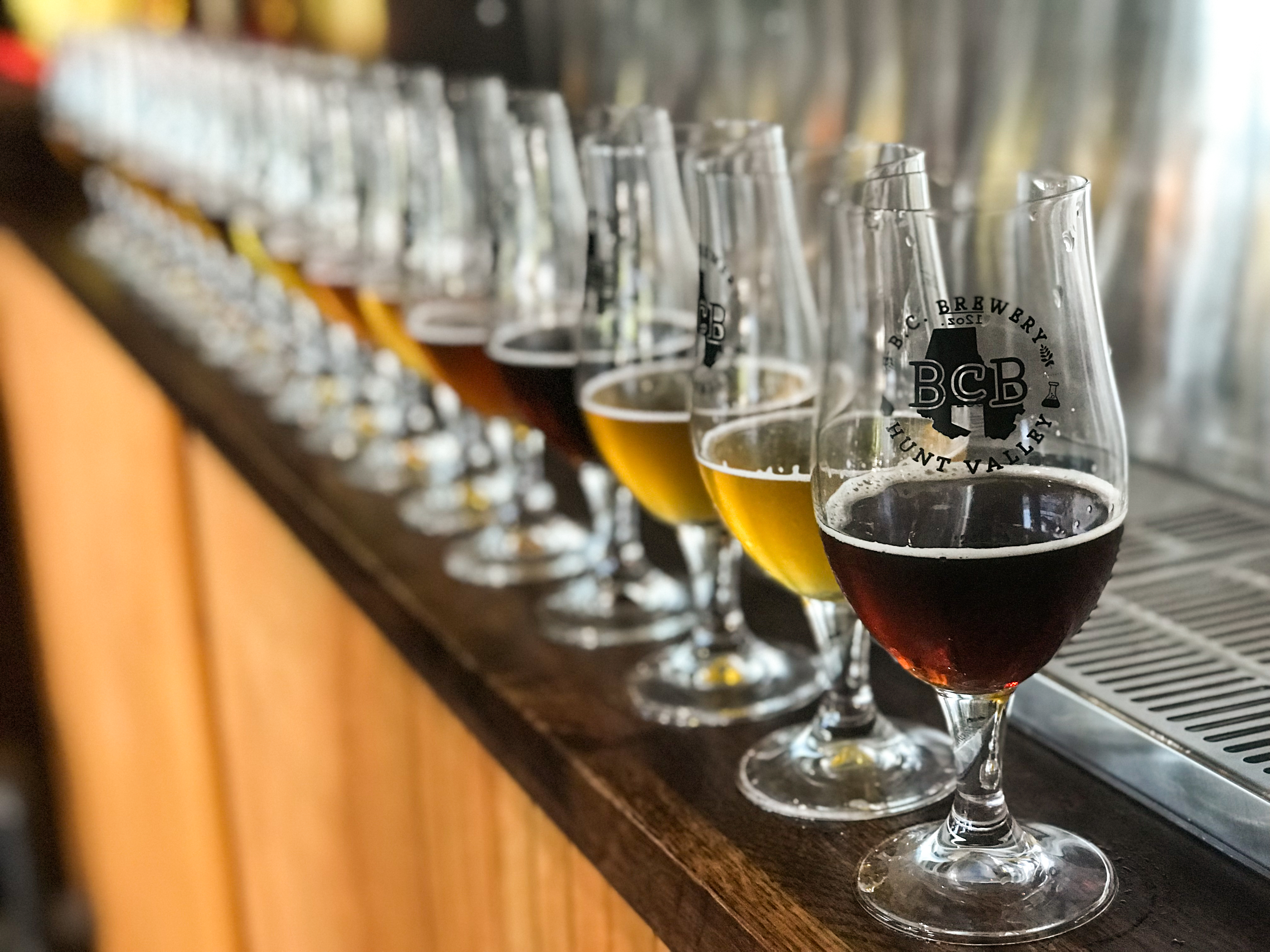 pic of a line of 20 glasses of beer with various style and colors of beer, poured to 2 ounces, each. They are on the counter at the self serve wall