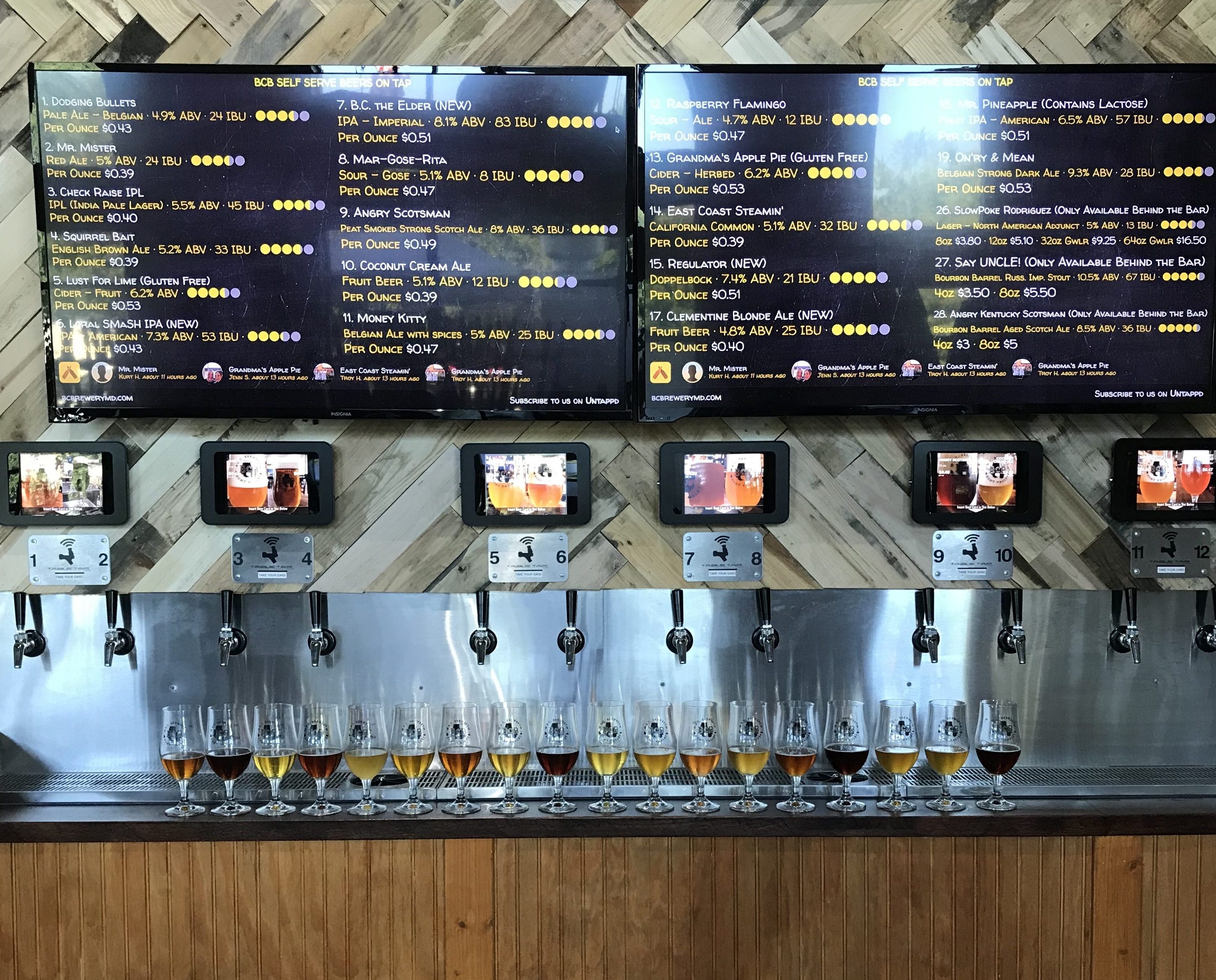 pic looking at the self serve wall with 2 menu tvs above 12 taps. A line of glasses with various beers are on the counter in front of the taps